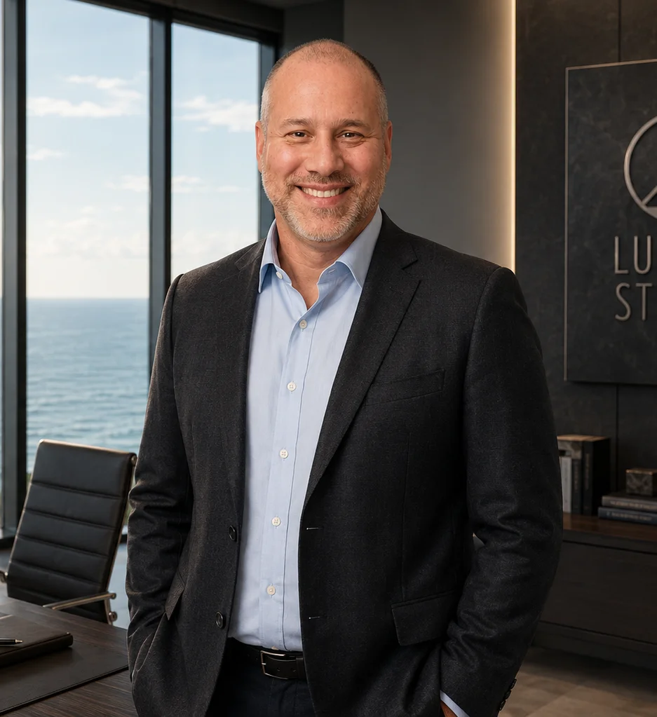 Portrait of Lucent Steele, smiling in a dark blazer and light blue shirt in an office overlooking the ocean.